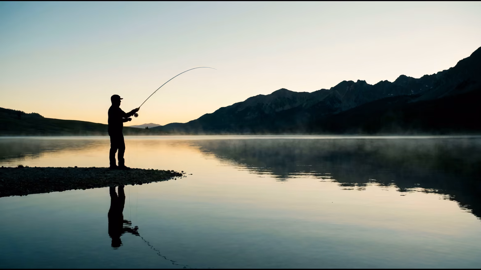 Ein Angler als Silhouette an einem stillen Bergsee im ersten Licht wirft aus; die Fliege landet und Ringe laufen über das Wasser.
